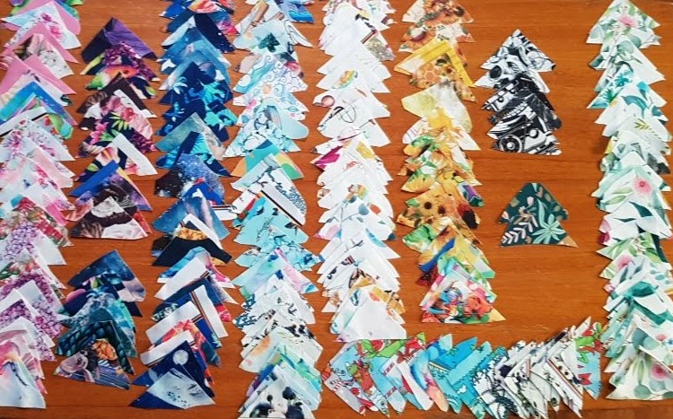 Colourful pieces of material cut into small triangles, laid out, on eachother in rows, in colour groups