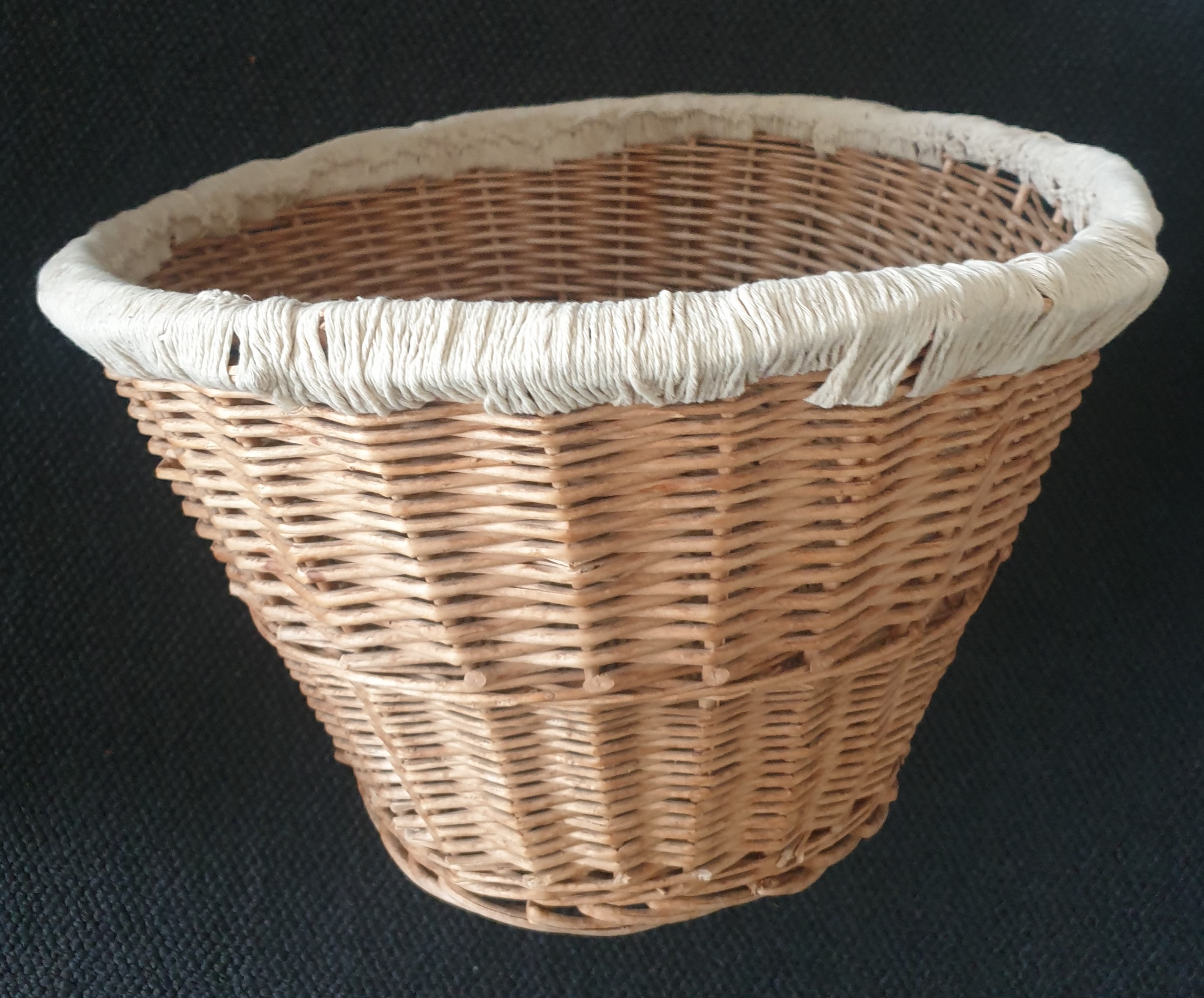 Side view of a wicker basket with crochet edging completed in a tan colour. There are no visible handles.