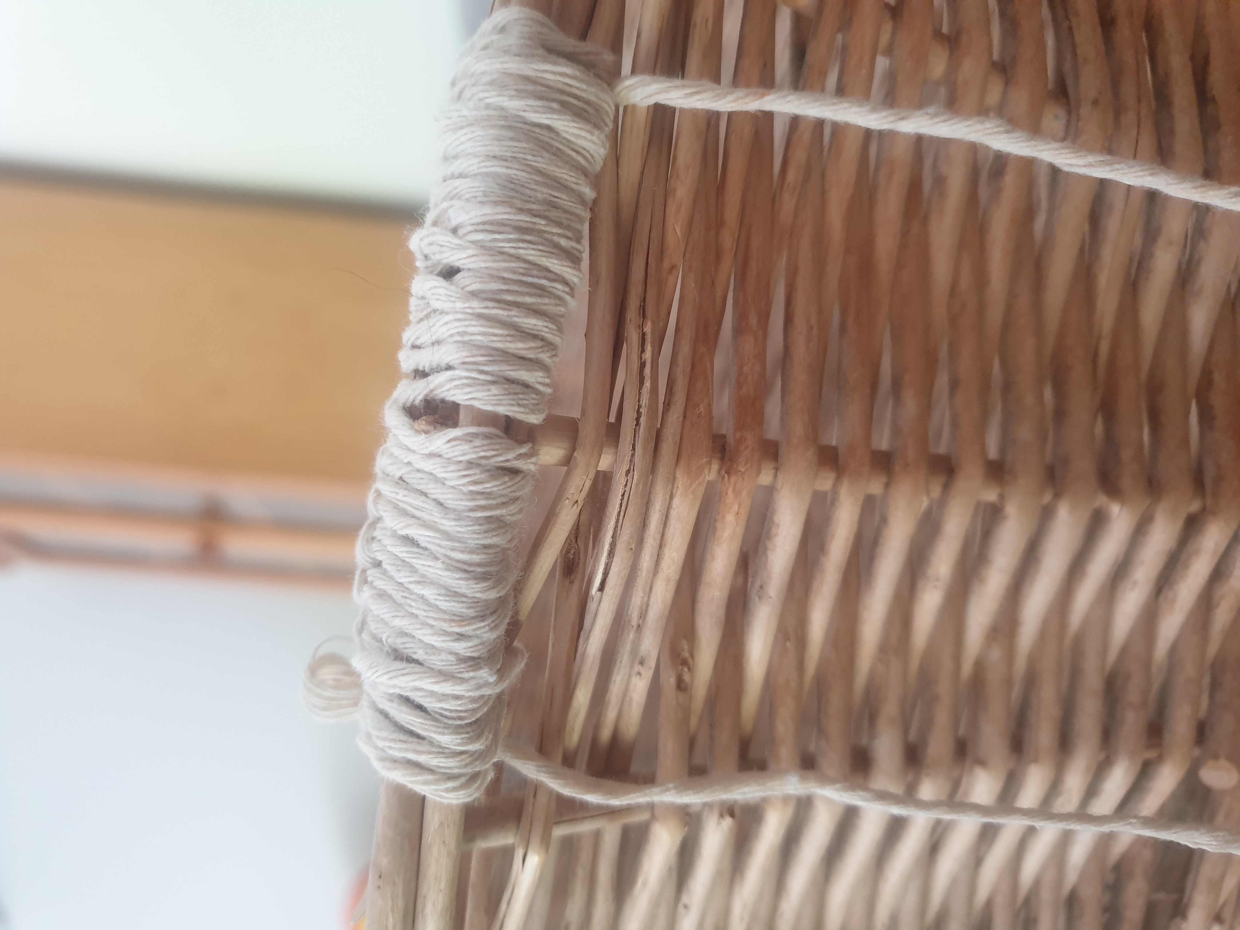 Close up of the outside of a wicker basket which has about 10cm of beige yarn crocheted on the top edge.